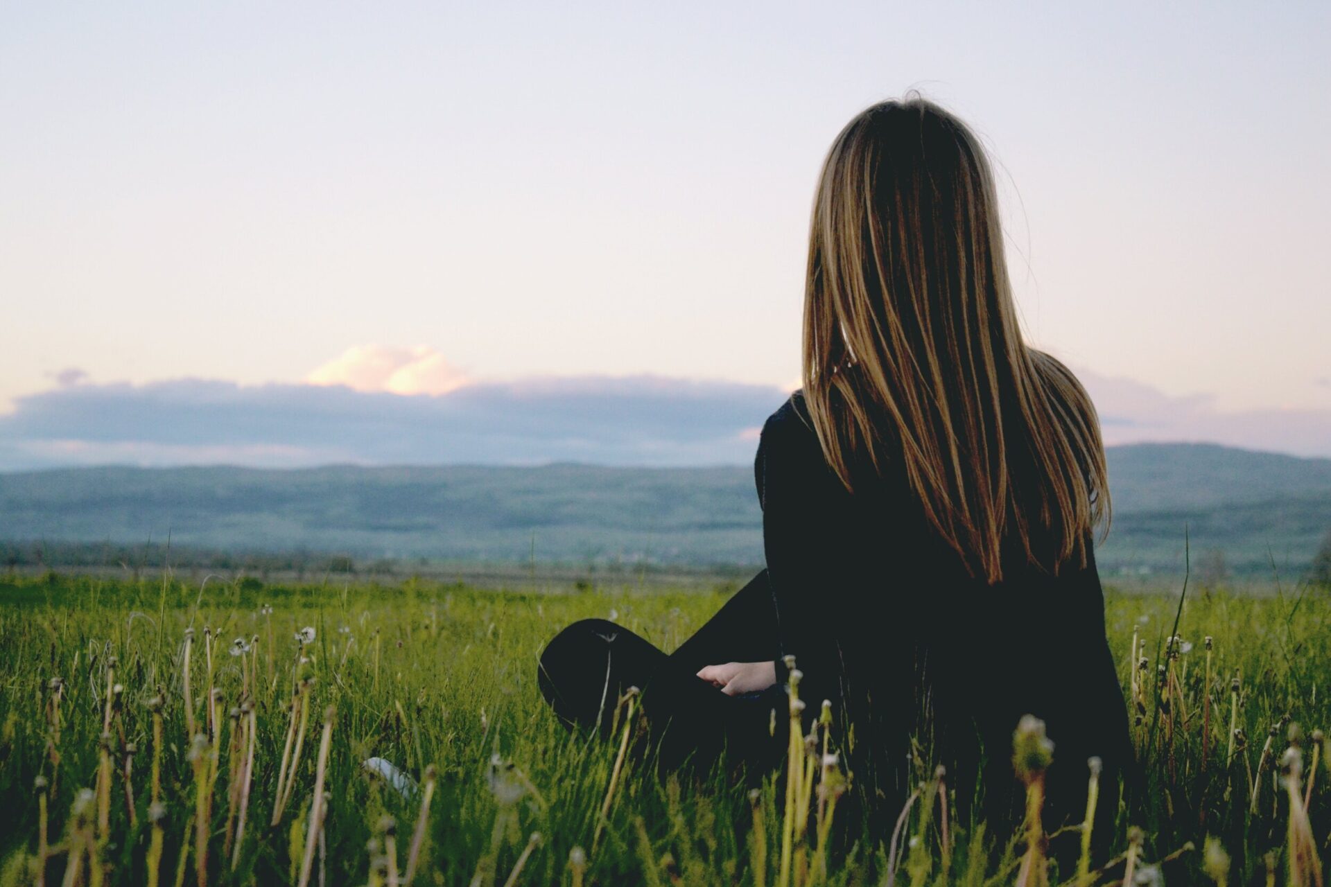 woman sitting in field looking at mountains