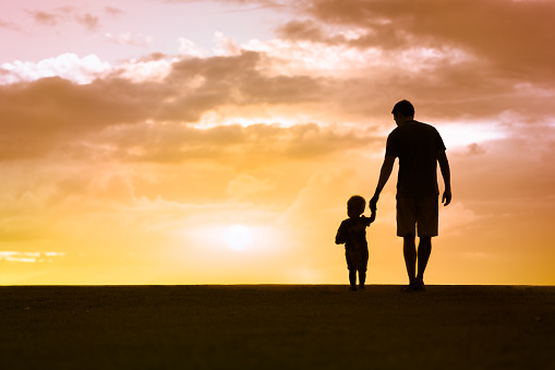 Loving father walking side by side with son holding hands.