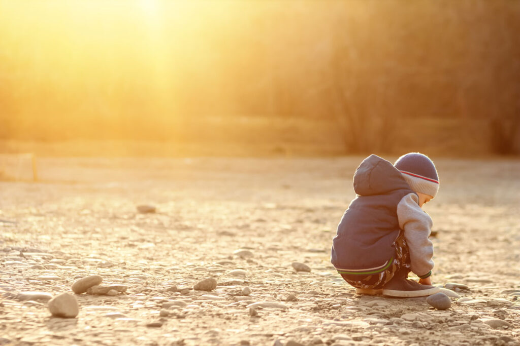 Young boy with autism sits on the ground alone at sunse