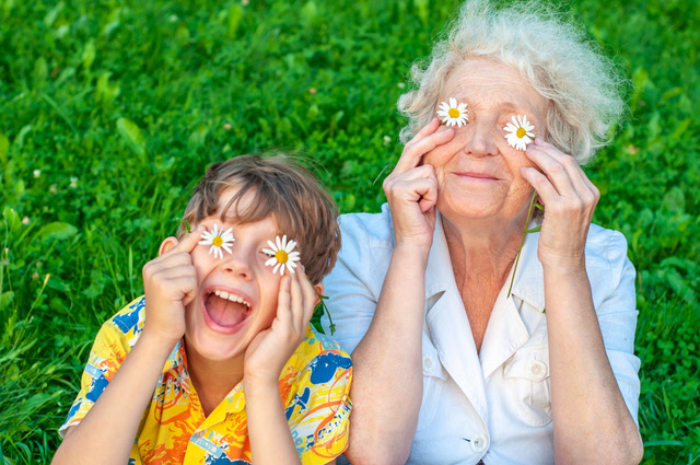 Happy grandmother and grandchild fooling around the law of putting chamomiles instead of eyes. Family love and relationships.